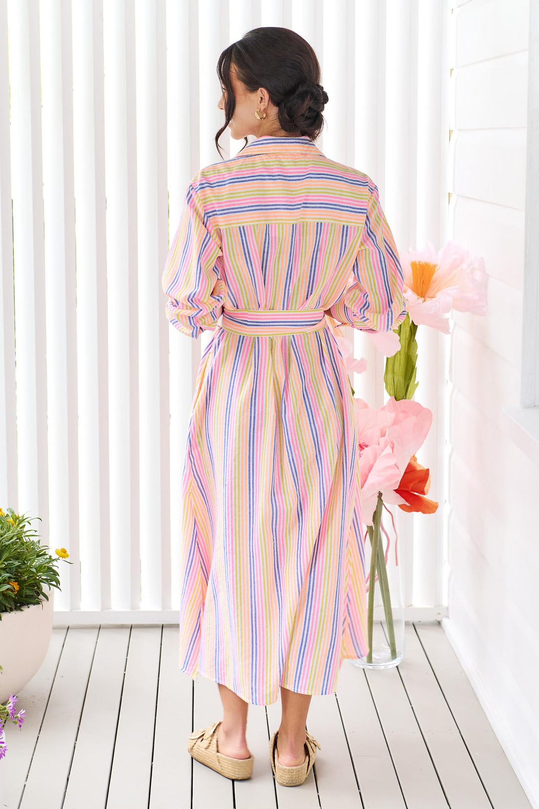 Back view of a woman wearing the minnie + MAXXIE Rio midi dress with 3/4 sleeves, colourful neon stripe print and a tie at the waist.