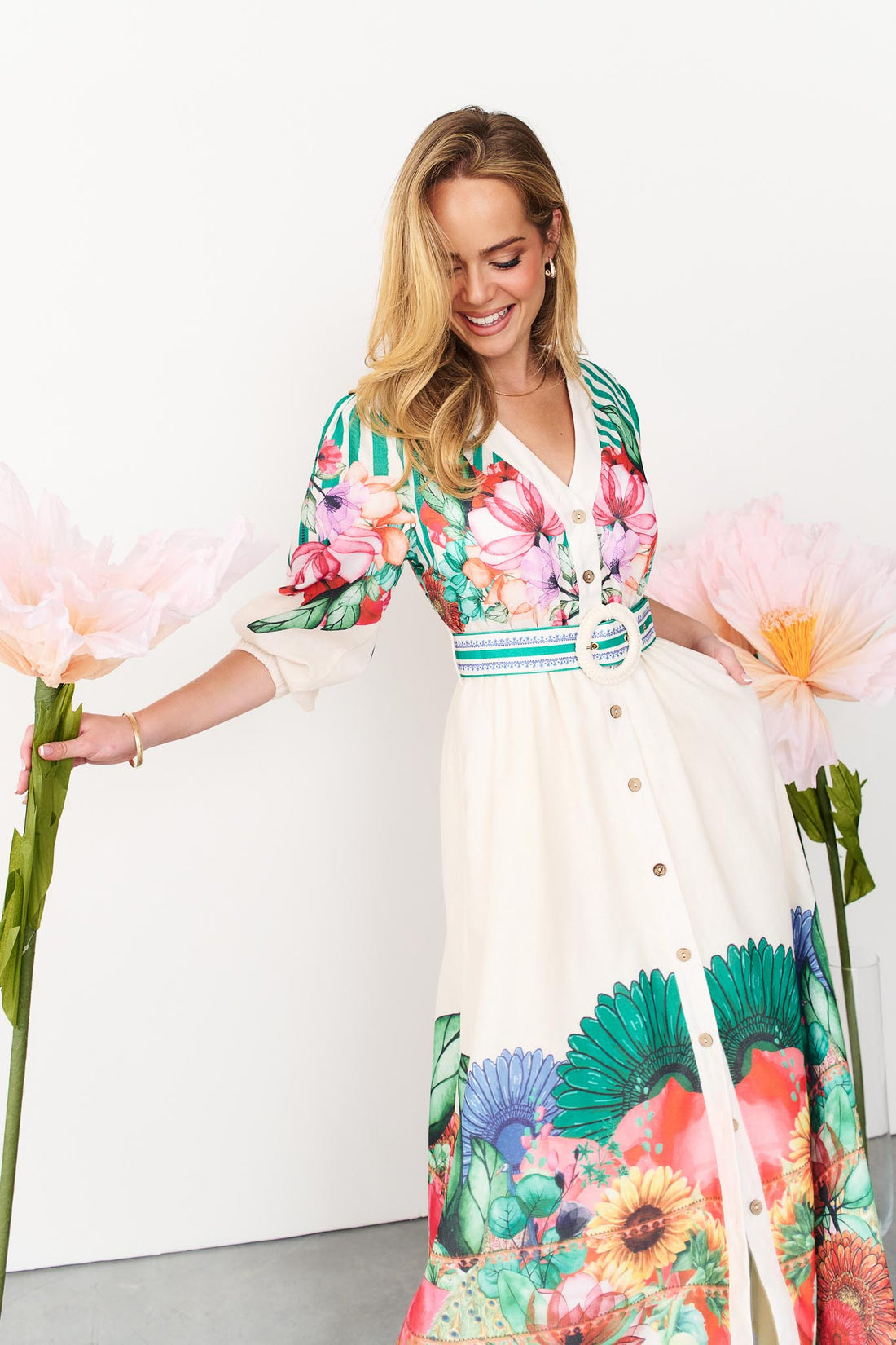 Rosabella maxi shirt dress with a bright floral and stripe print and white crochet buckle belt with a model holding giant pink flowers