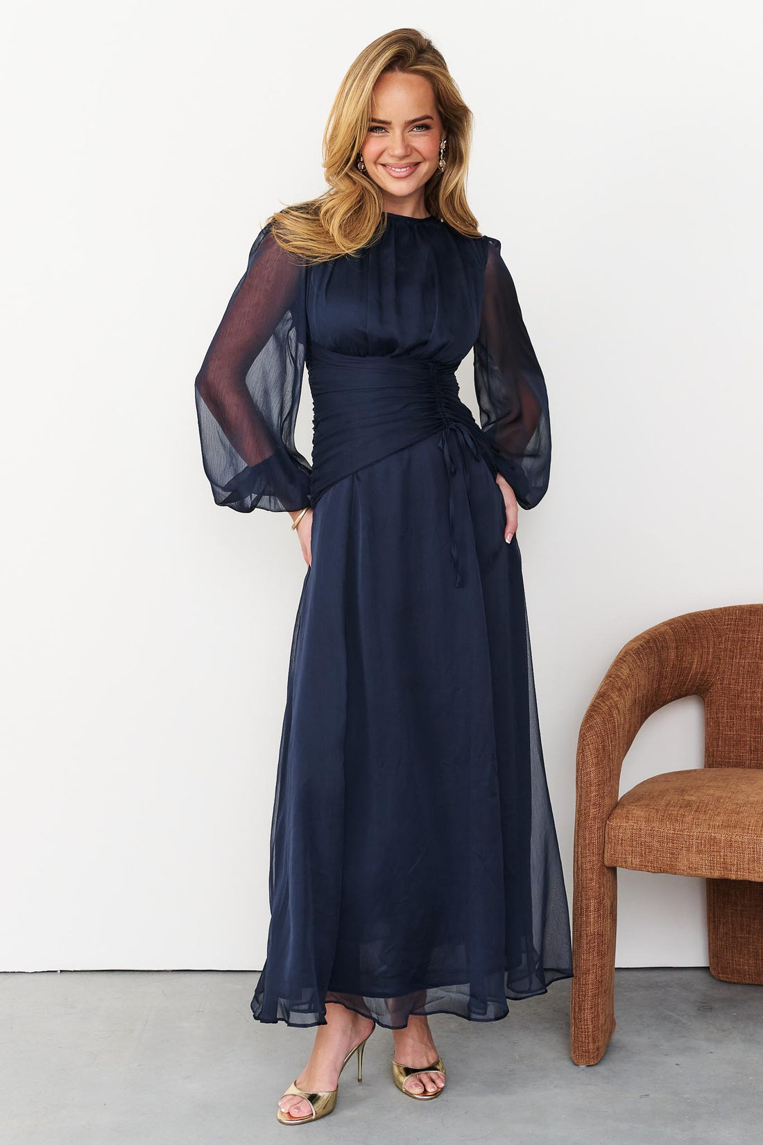 Sabine maxi event dress in navy blue with a ruched waist and long sheer sleeves.
