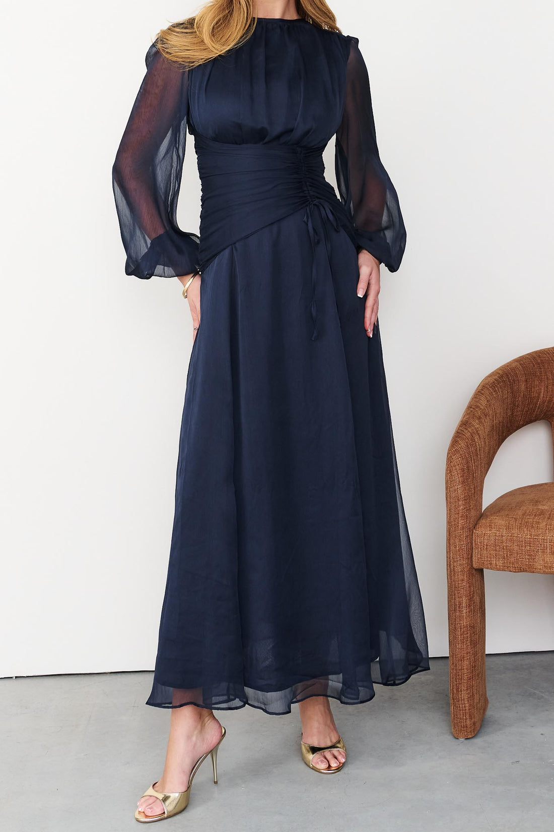 Full length image of Sabine maxi event dress in navy blue with a ruched waist and long sheer sleeves.