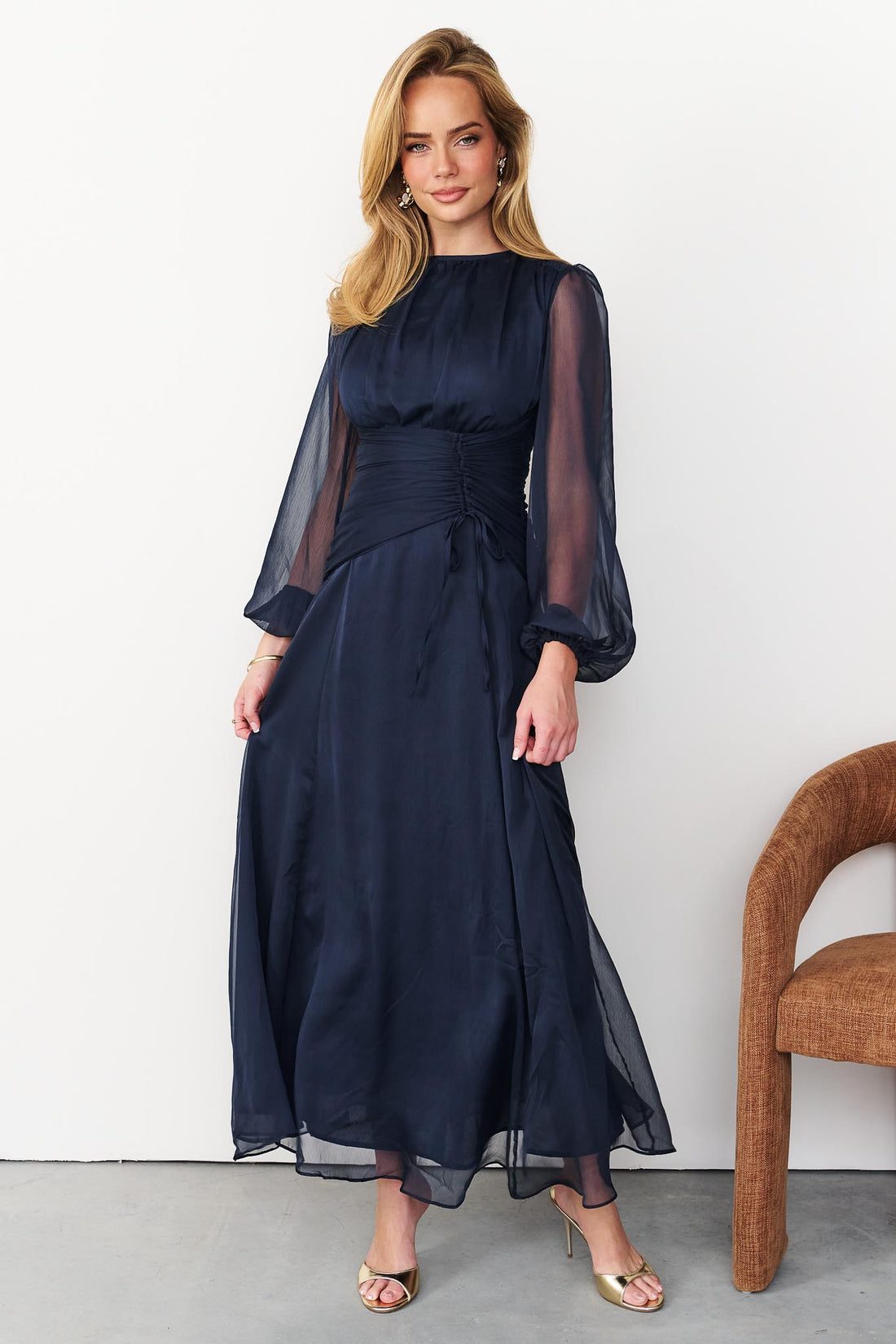 Sabine maxi event dress in navy blue with a ruched waist and long sheer sleeves.