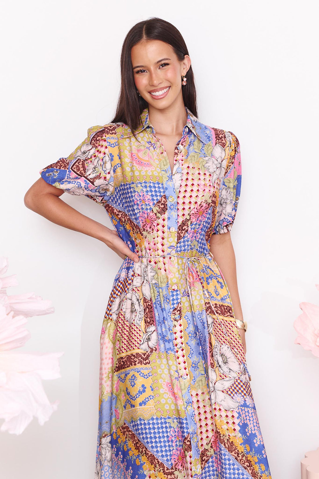Detail of a woman wearing the minnie + MAXXIE Sabrina short-sleeved maxi dress with a colourful patchwork print. The dress features a mix of blue, pink, yellow, and white patterns.
