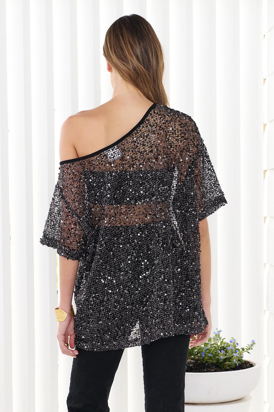 Back view of woman wearing a black sequin off-shoulder top with black jeans