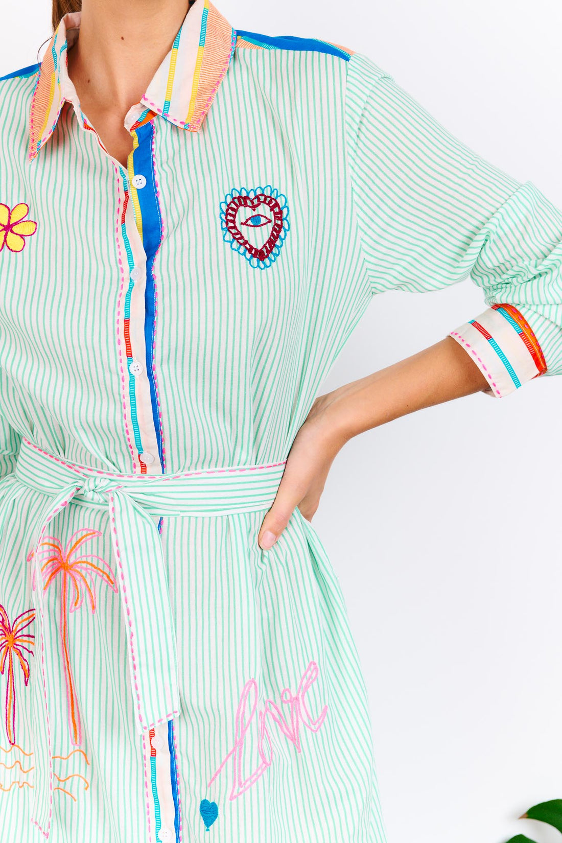 Detail of the minnie + MAXXIE Summer Love Cotton shirt dress with a green pinstripe print, colourful embroidery details and a matching waist tie.