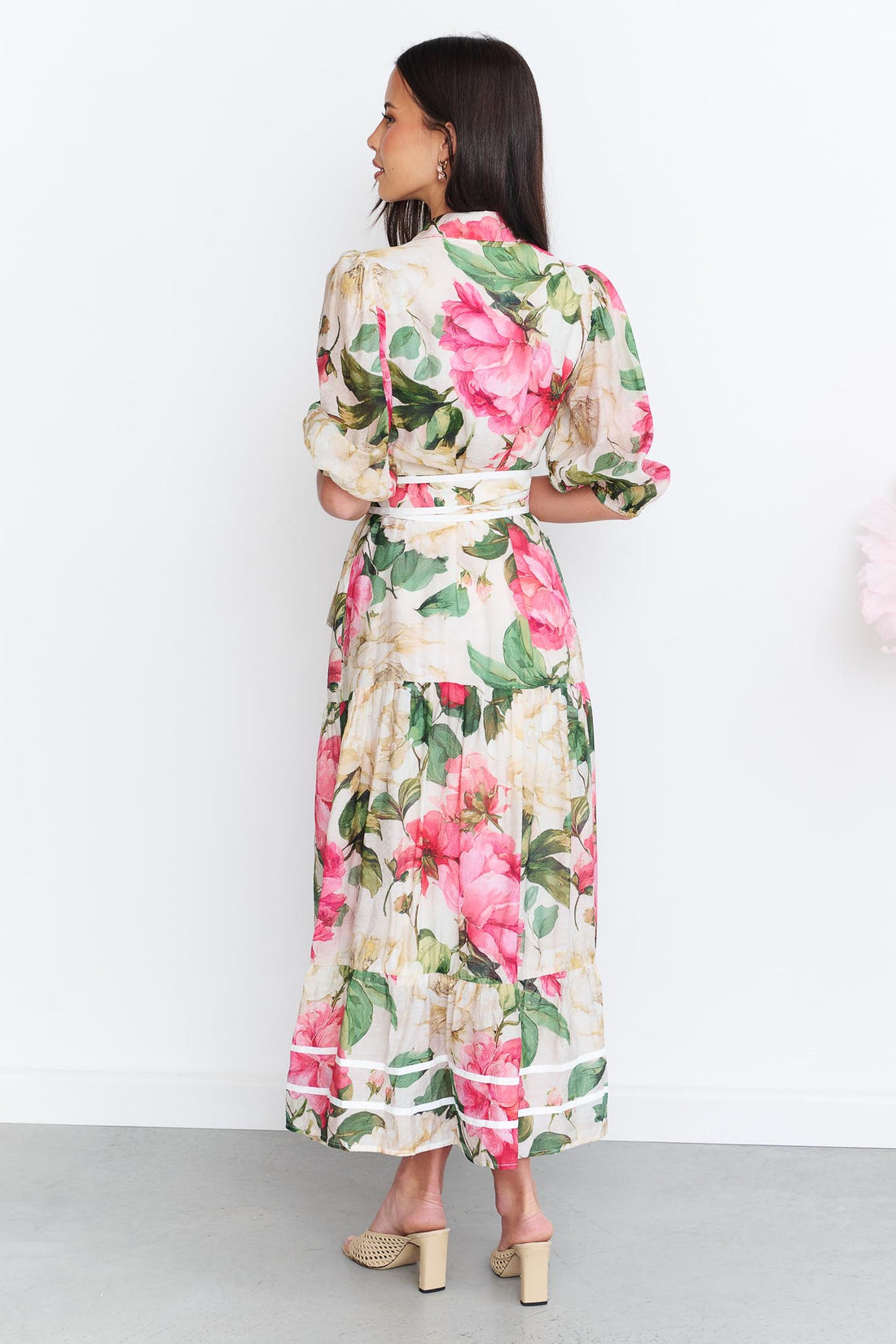 Back view of a woman wearing the minnie + MAXXIE Valois maxi shirt dress with a vibrant pink and green floral print. The dress features a matching fabric waist tie, and short puff sleeves.