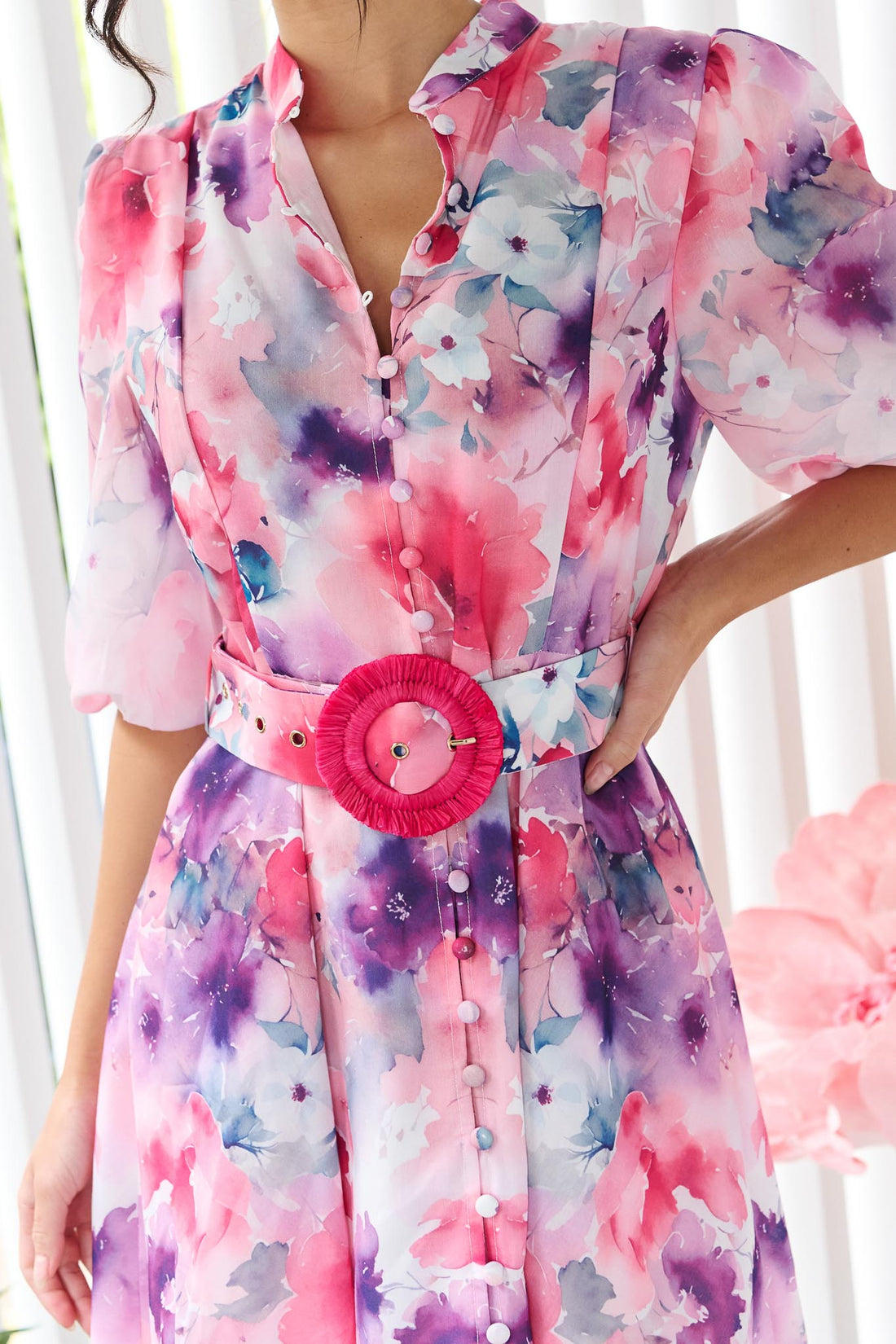 Detail of a woman wearing the minnie + MAXXIE Willow Bloom midi dress with puff sleeves and a pink and purple watercolour print with pink raffia belt.